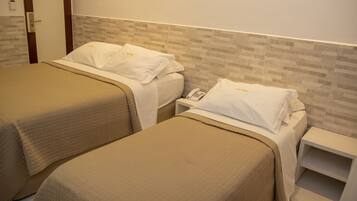 A hotel room with two beds, each with a quilted bedspread and white pillows. There is a bedside table with a phone and a small shelf.