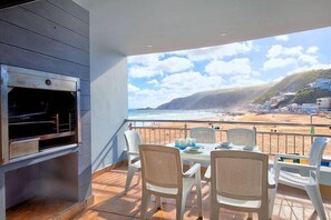 A balcony with a grill, dining table, and chairs overlooking a beach. - Makarios on Sea (Herolds Bay)