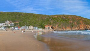 A beach with houses in the background and people enjoying the water. - Makarios on Sea (Herolds Bay)