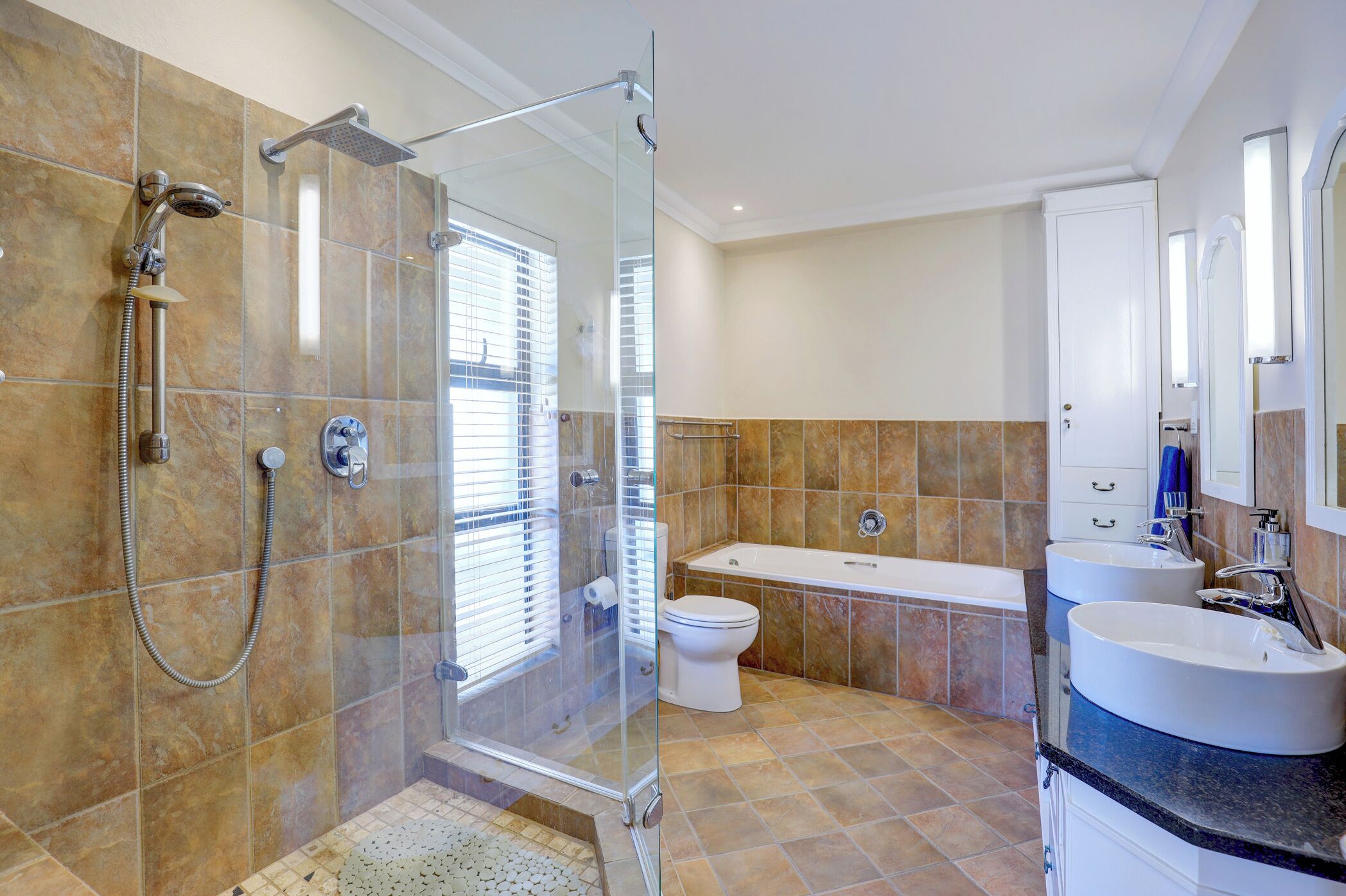 Un baño moderno con ducha de vidrio, bañera y dos lavamanos.