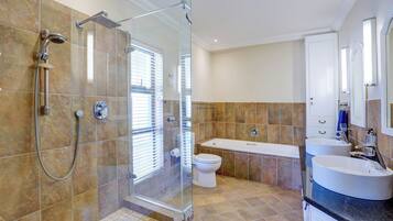 Un baño moderno con ducha de vidrio, bañera y dos lavamanos.