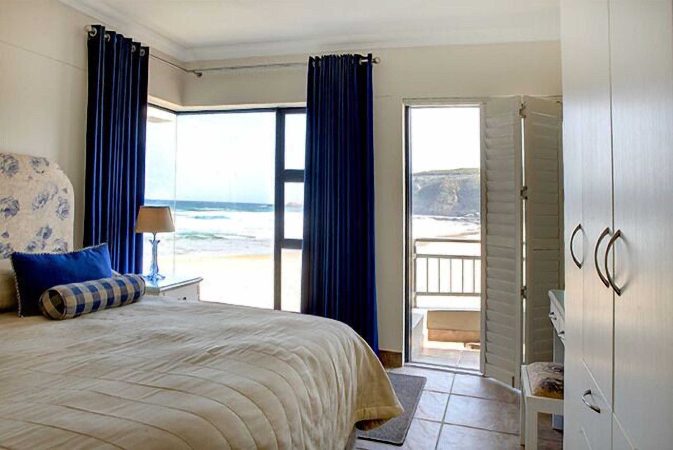 Une chambre à coucher avec un lit, une table de chevet, une lampe, une vue sur l’océan et un balcon.