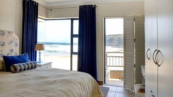 A bedroom with a bed, a nightstand, a lamp, a view of the ocean, and a balcony.