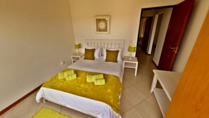 A neatly arranged hotel room with a bed, two bedside tables, and a nightstand. - Moringa Gardens (Swakopmund)