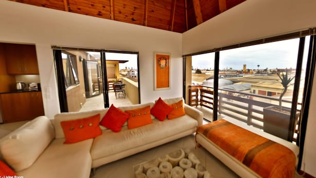 A living room with a sofa, a coffee table, and a view of the city through large windows. - Moringa Gardens (Swakopmund)
