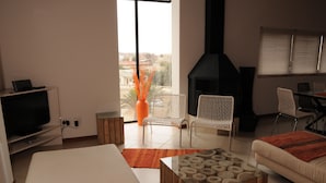A living room with a TV, sofa, chairs, a fireplace, and a view of the city. - Moringa Gardens (Swakopmund)