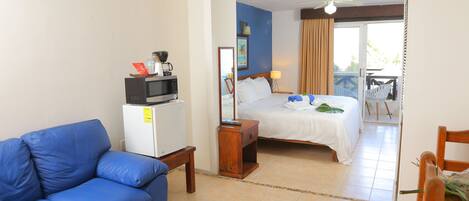 Habitación de hotel con sofá azul, cama, una mesita, microondas y balcón con vistas.