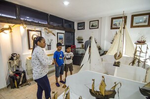 Quarto com um grande modelo de veleiro, um esqueleto e quadros nas paredes.