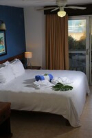 Habitación de hotel con una cama grande, ventilador de techo, ventana con cortinas y vistas al exterior.