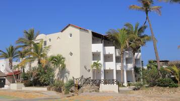 Un edificio de varios pisos con balcones, rodeado de palmeras y un cielo azul despejado.