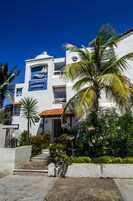 A white building with a blue mural, palm trees, and colorful flowers.