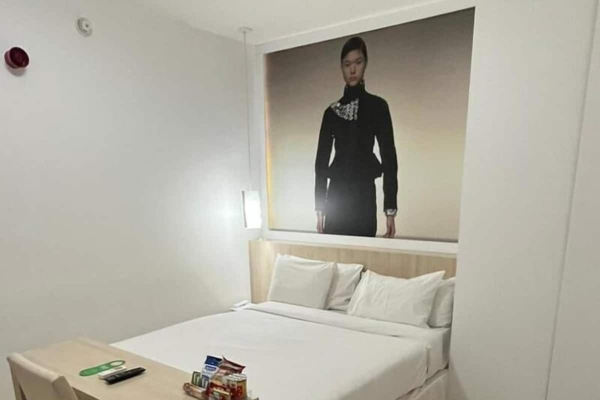 Hotelkamer met een bed, een bureau en een stoel. Er hangt een poster aan de muur en op een klein tafeltje staan spullen.