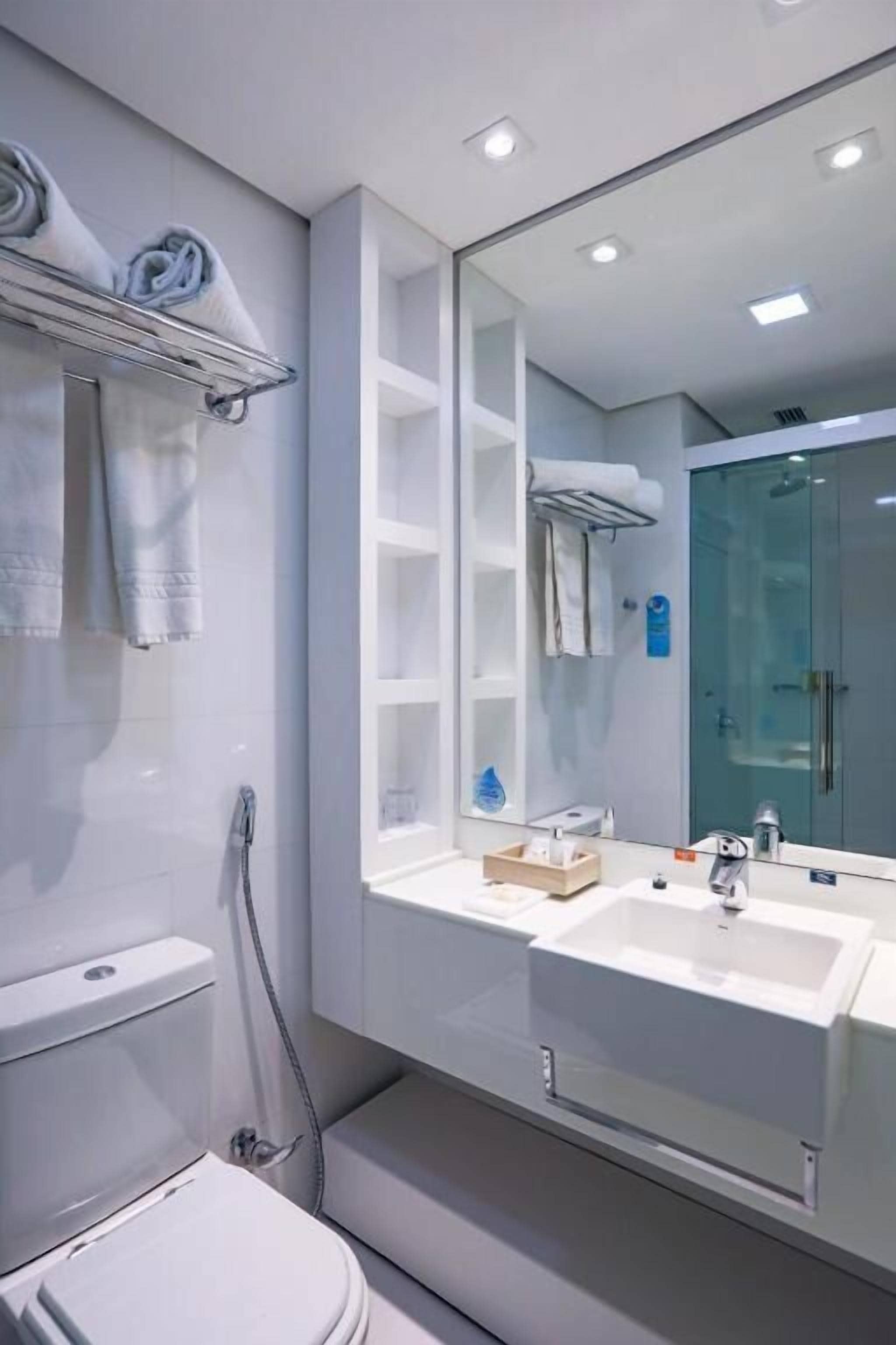 A modern bathroom with a large mirror, two sinks, a toilet, and a shower.