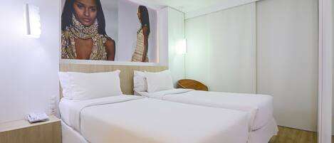 A hotel room with two beds, a nightstand, a wall-mounted mirror, and a large poster.
