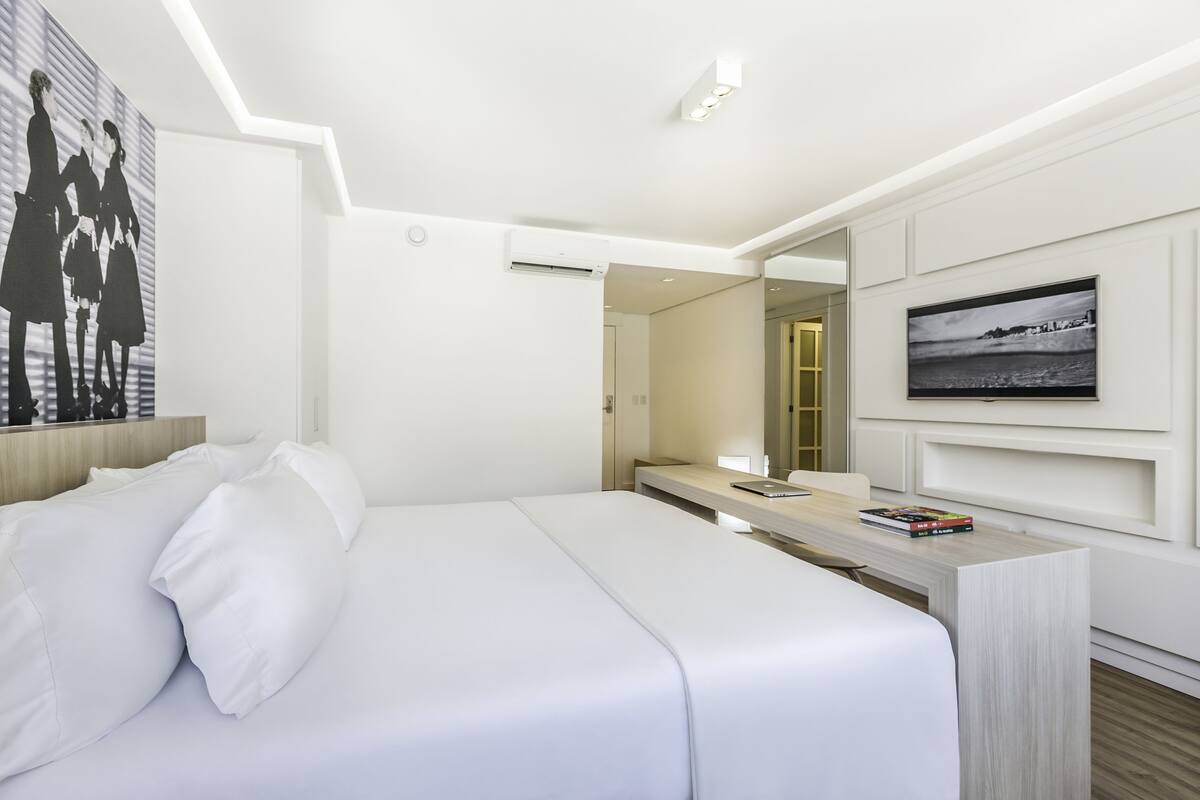 Een moderne hotelkamer met een groot bed, een bureau met een laptop, een flatscreen televisie en een schilderij aan de muur.