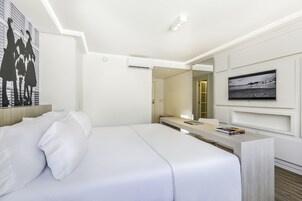 Una habitación de hotel moderna con una cama grande, un escritorio con una computadora portátil, un televisor de pantalla plana y un cuadro en la pared.