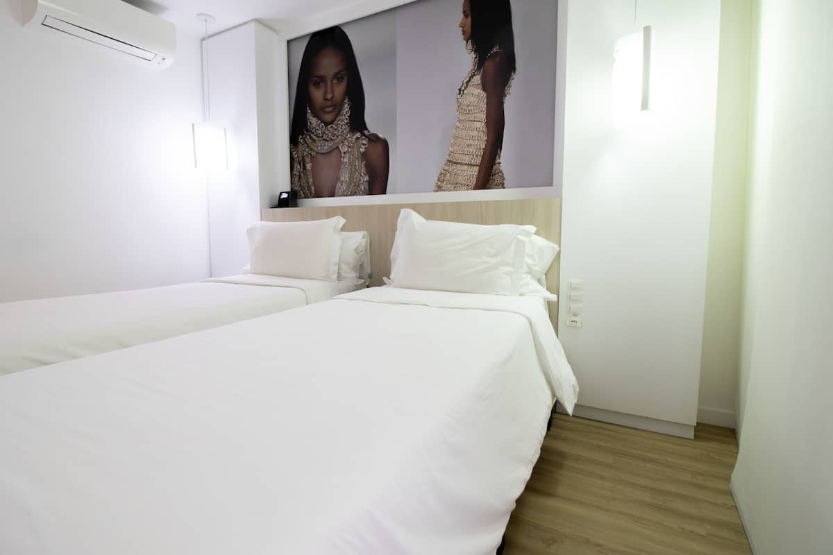 Een hotelkamer met twee eenpersoonsbedden, witte beddengoed, een grote spiegel en een luchtverfrisser aan de muur.
