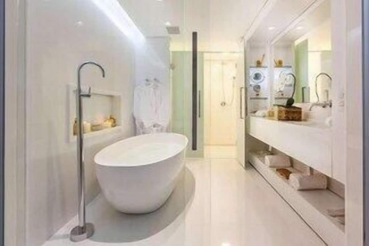 Een moderne badkamer met een vrijstaand bad, een douchecabine van glas en een wastafel met spiegel en handdoekhouder.