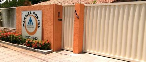 A hostel entrance with a sign indicating it is Manaira Hostel International, featuring a contact number and a gated entrance.