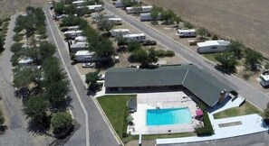 An aerial view of a campground with RVs, a swimming pool, and a large building with a sloped roof. - Lake Isabella RV Resort (Lake Isabella)