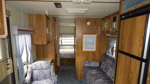 Ein kompaktes Wohnmobil-Interieur mit einer Küchenzeile, einem Bett und einer Sitzgruppe.