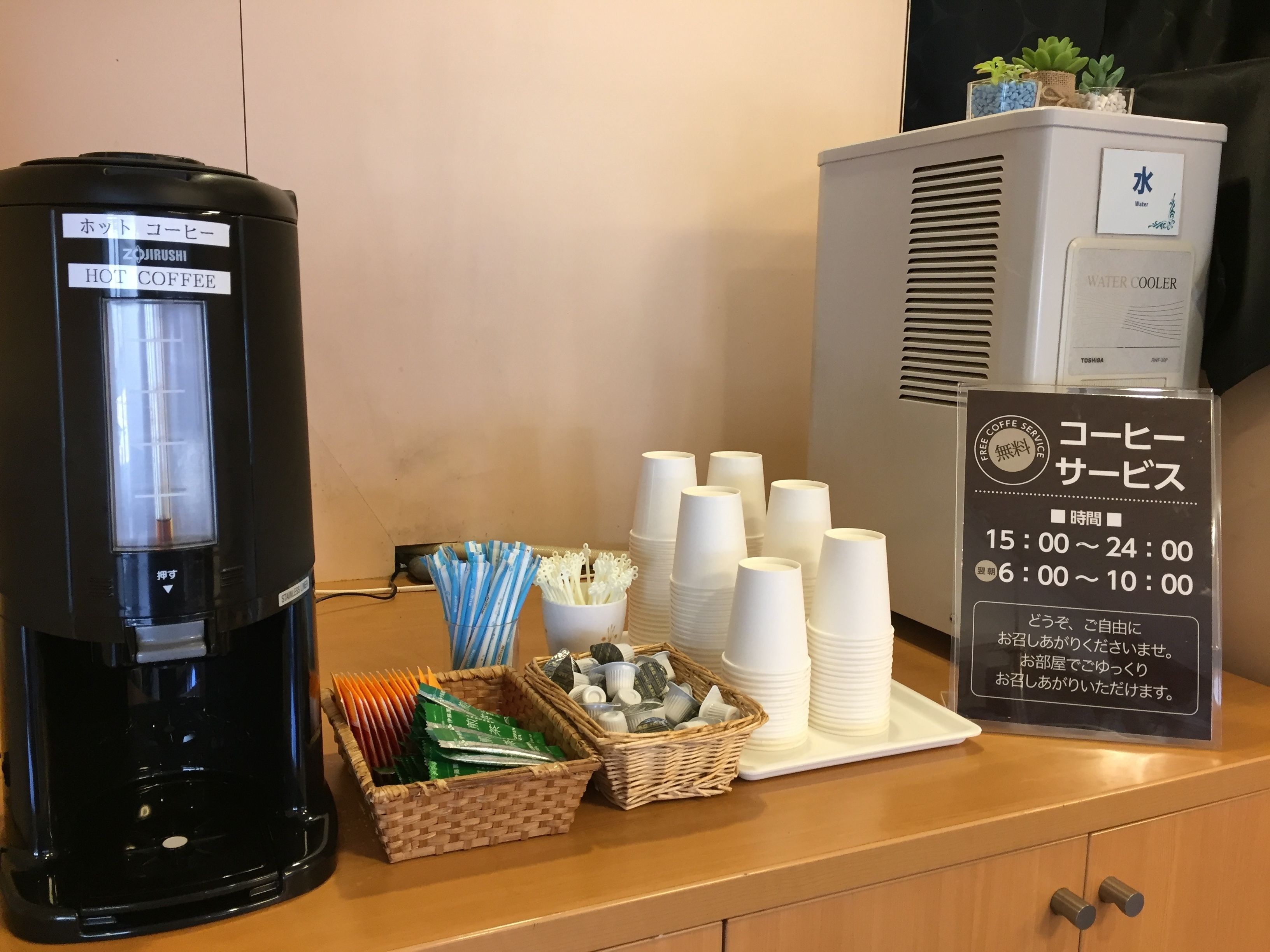 A coffee station with a hot coffee dispenser, a water cooler, and disposable cups.