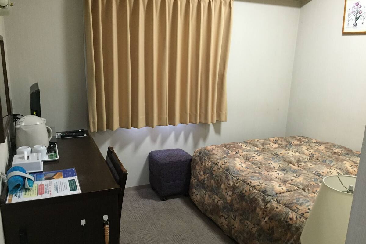 A hotel room with a bed, a desk with a kettle, cups, and a lamp.