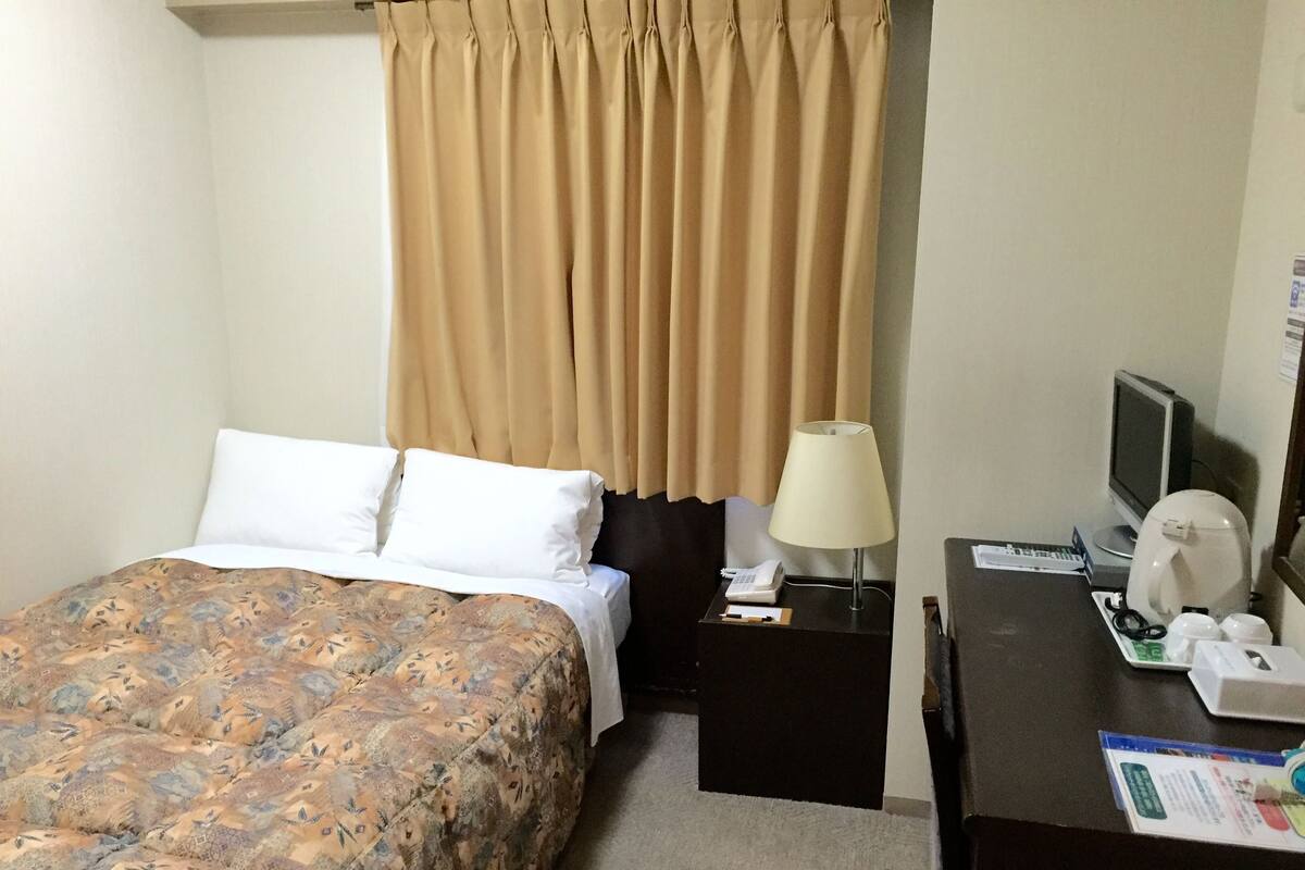 A hotel room with a bed, a desk with a computer, a telephone, and a coffee maker.