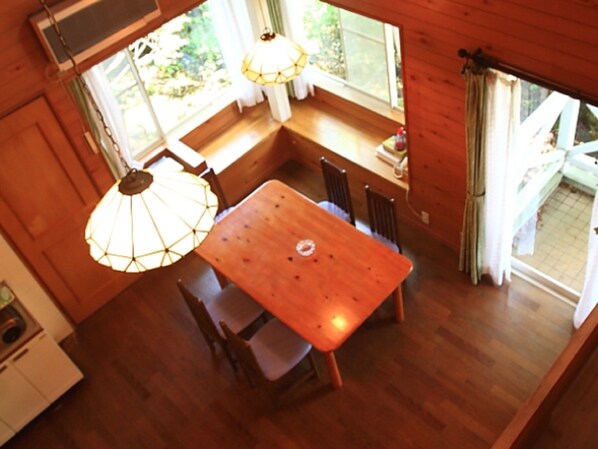 Una mesa de madera con sillas, un lámpara colgante y vistas al exterior a través de una ventana.