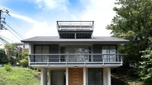 Een modern huis met twee verdiepingen, een balkon, een houten deur en een kleine tuin.