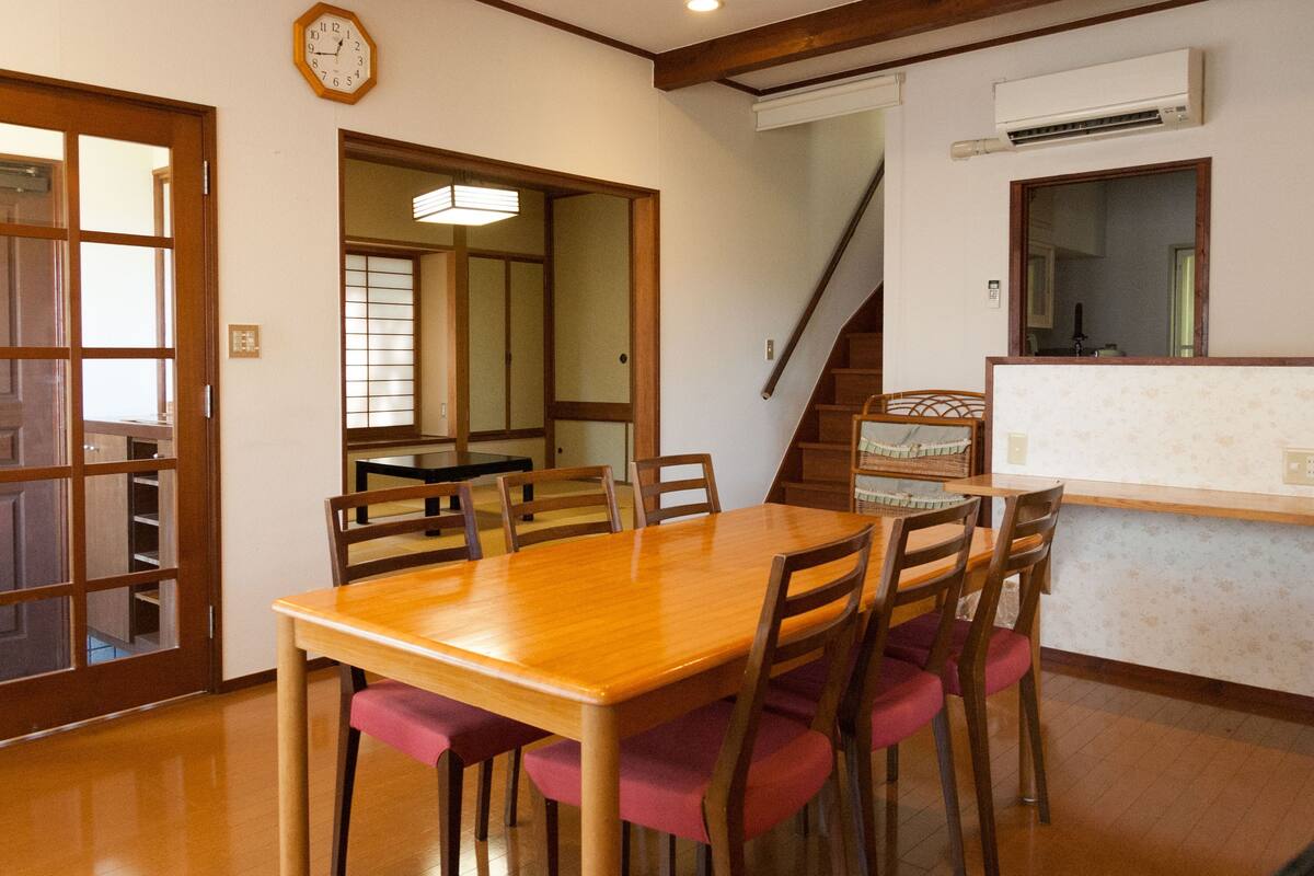 Een eethoek met een houten tafel en stoelen, een trap en een keuken met een aanrecht en spoelbak.