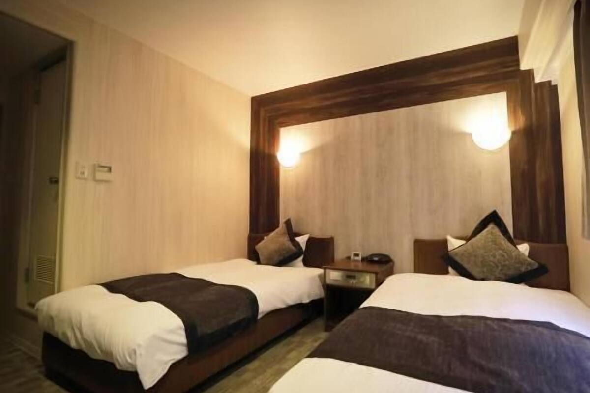 A hotel room with two beds, a wooden headboard, a nightstand, and a mirror.