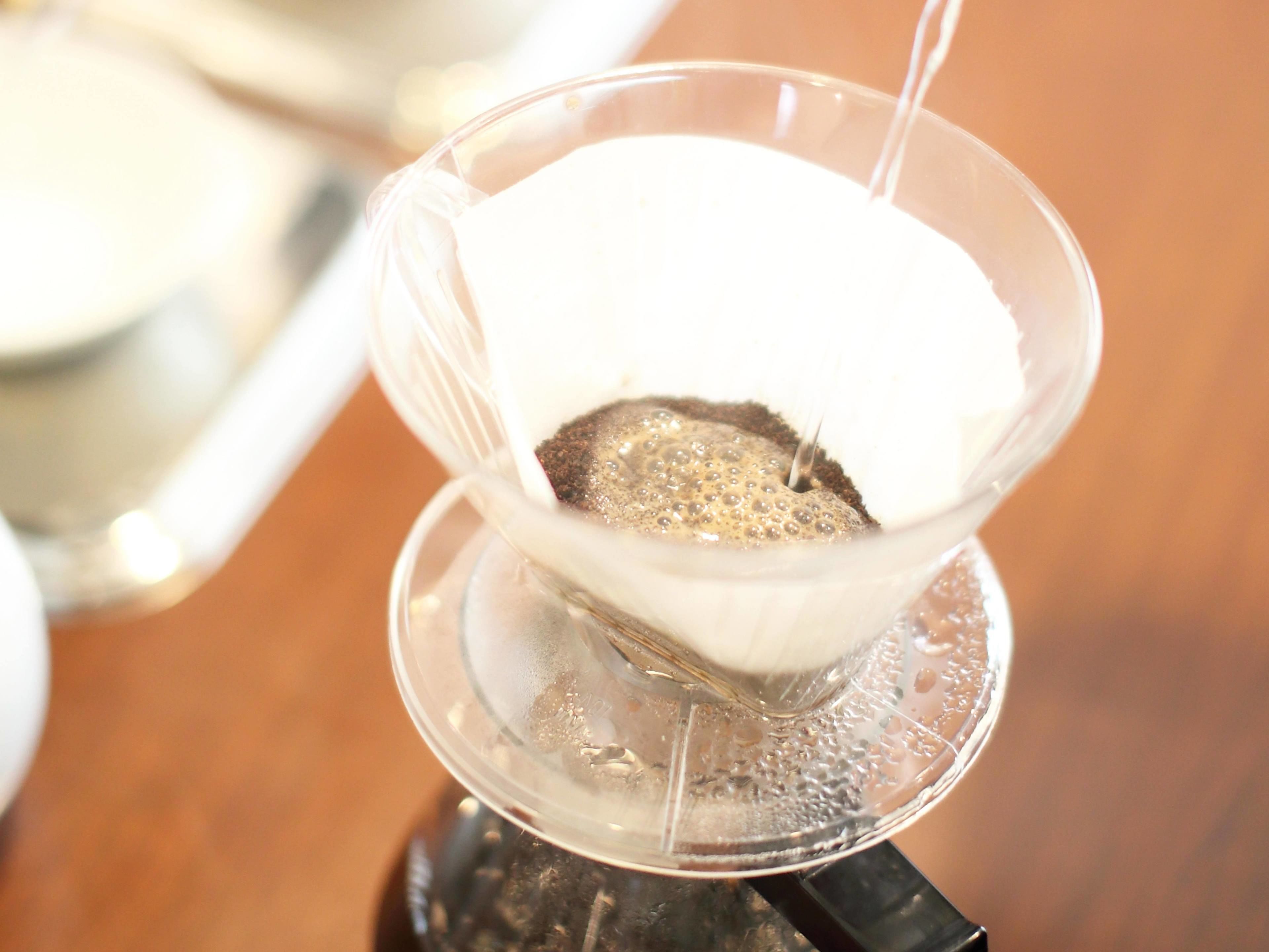 A clear glass coffee pot with a filter, placed on a stand.