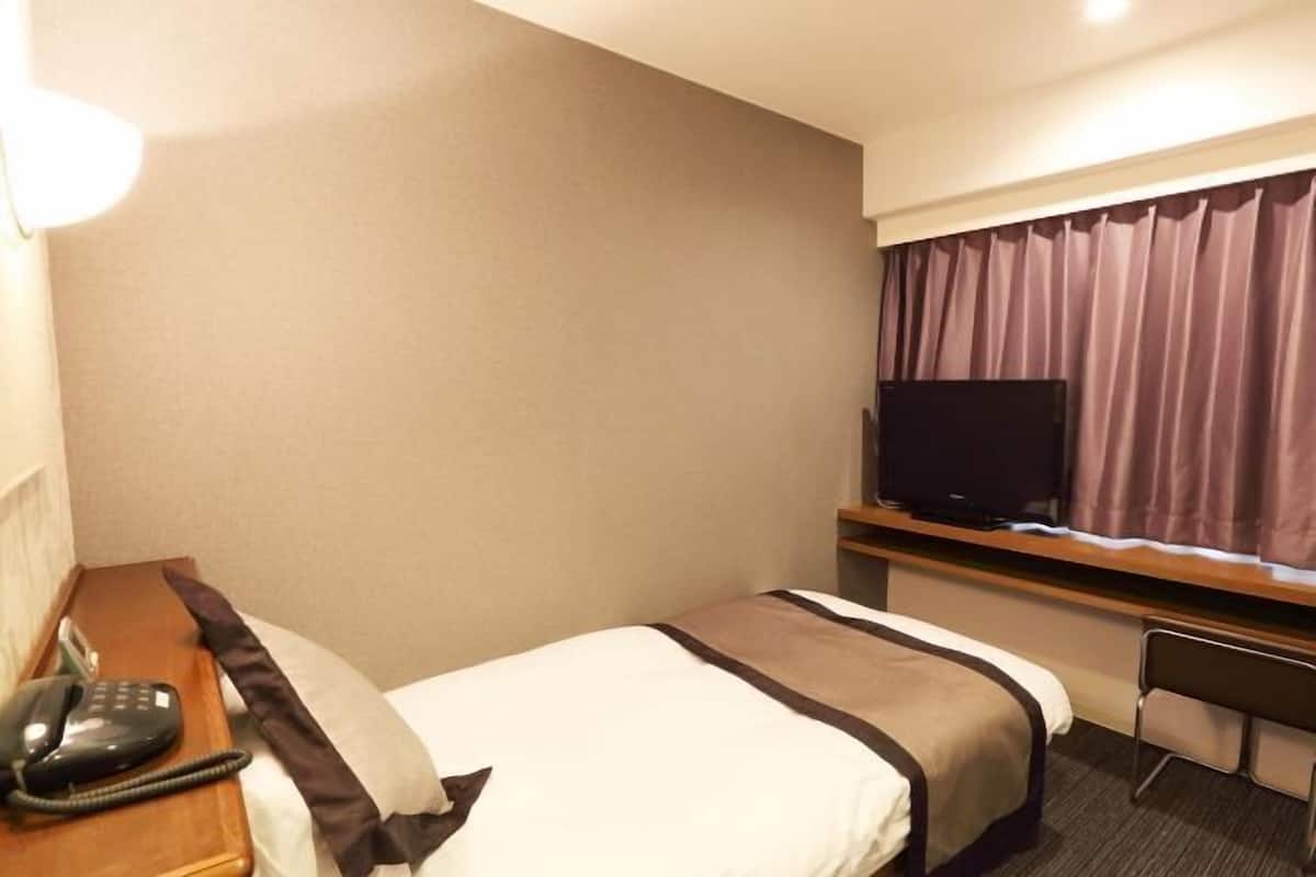 A hotel room with a bed, a desk, a television, and a telephone.