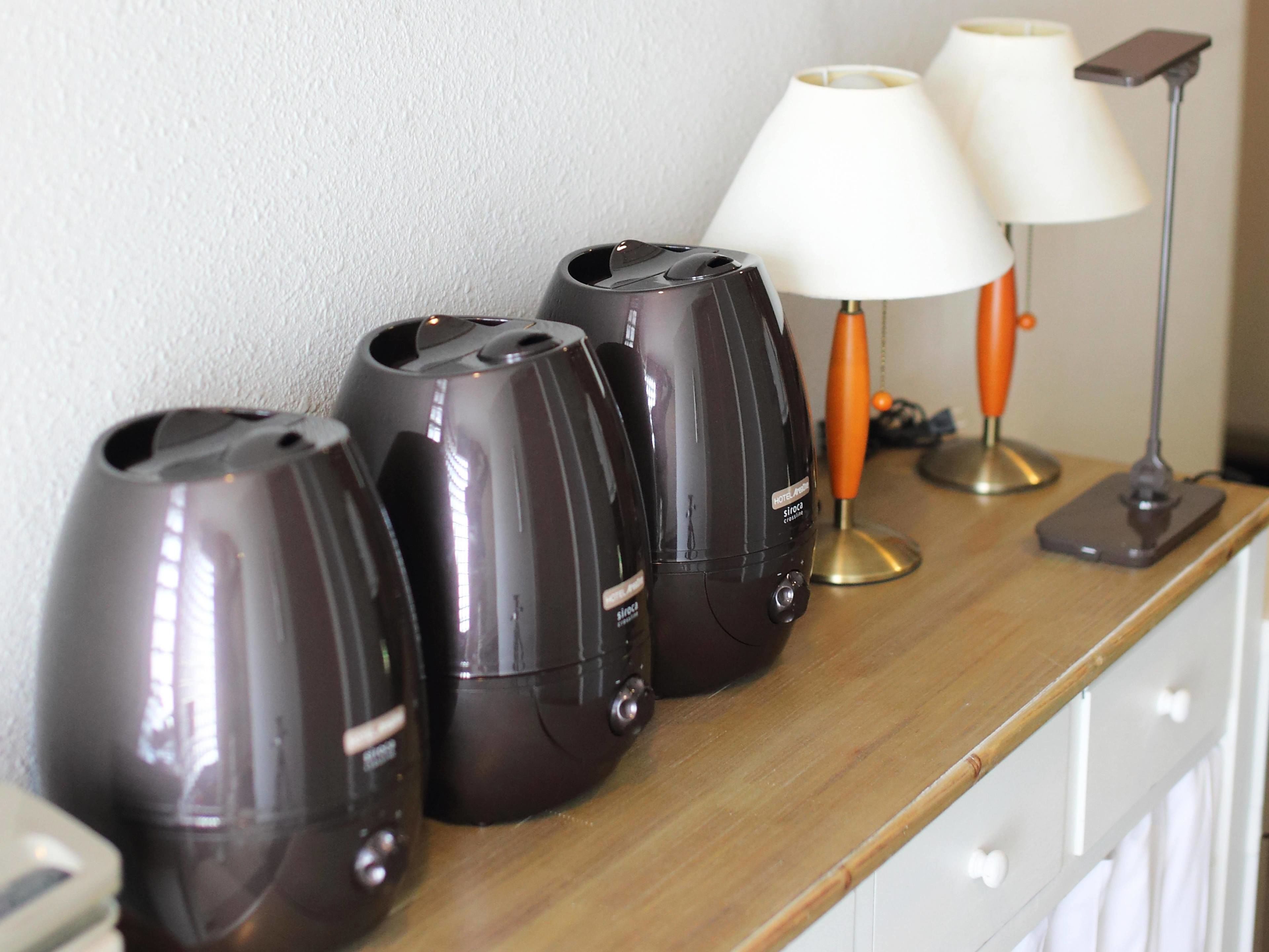 A wooden table with four black electric kettles, two white lamps, and an orange lamp.