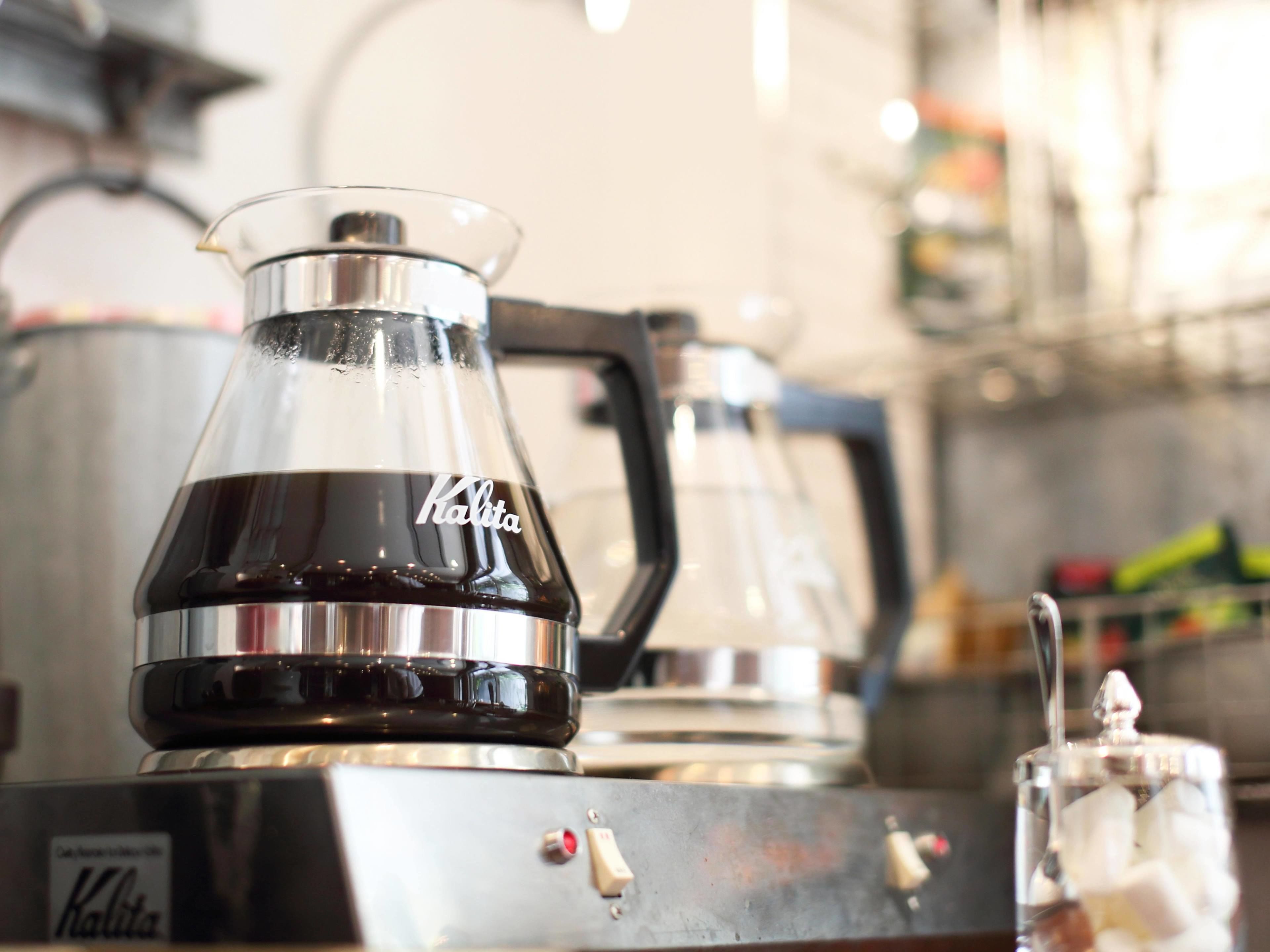 A coffee maker with a clear glass carafe and a metal handle, labeled 'Kalita'.