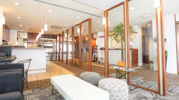 En moderne hotellobby med receptionsdisk, siddeområde og et stort spejl der reflekterer indretningen.