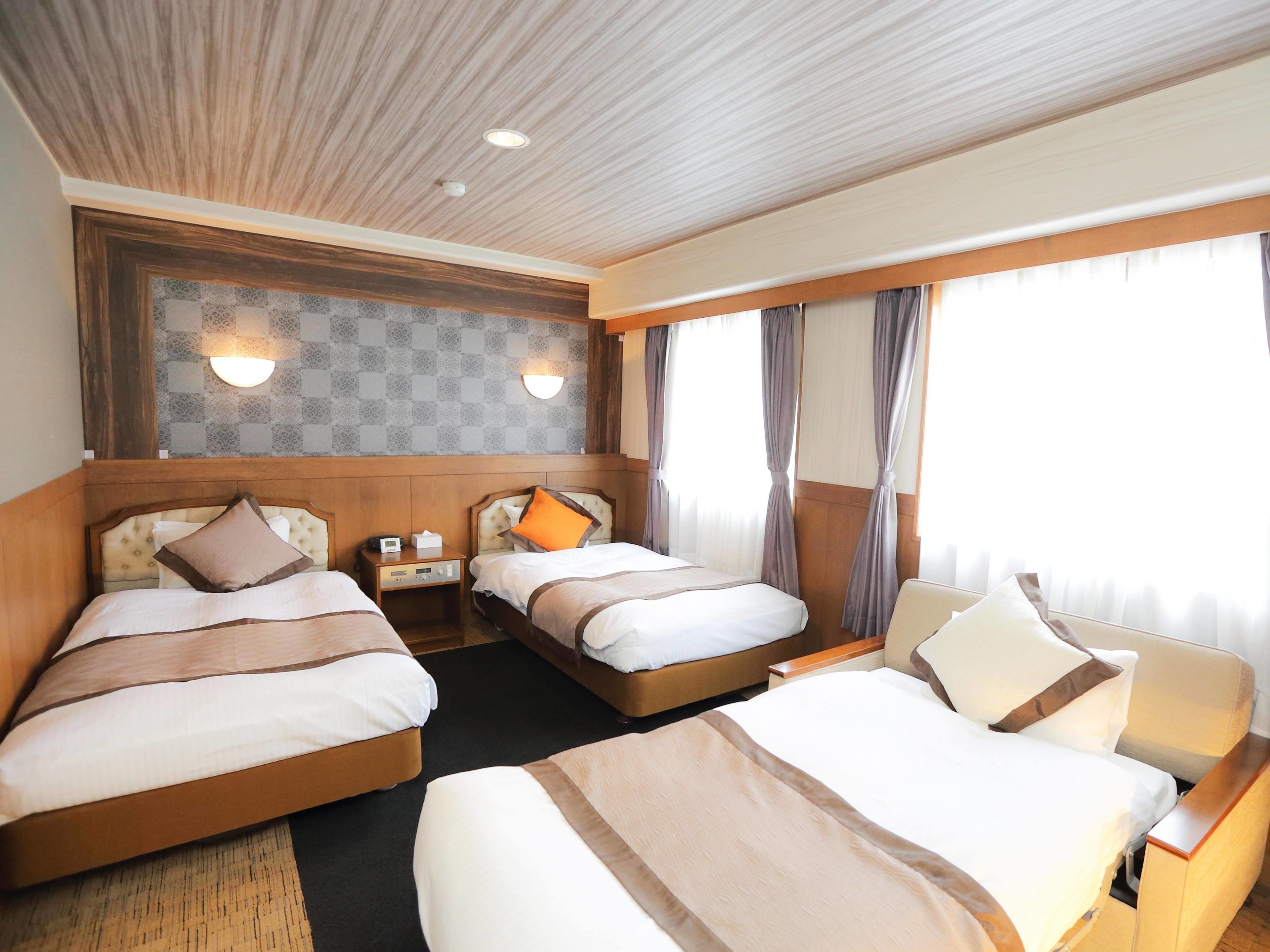 A hotel room with two beds, a nightstand with a lamp, a wall-mounted light, and a window with curtains.