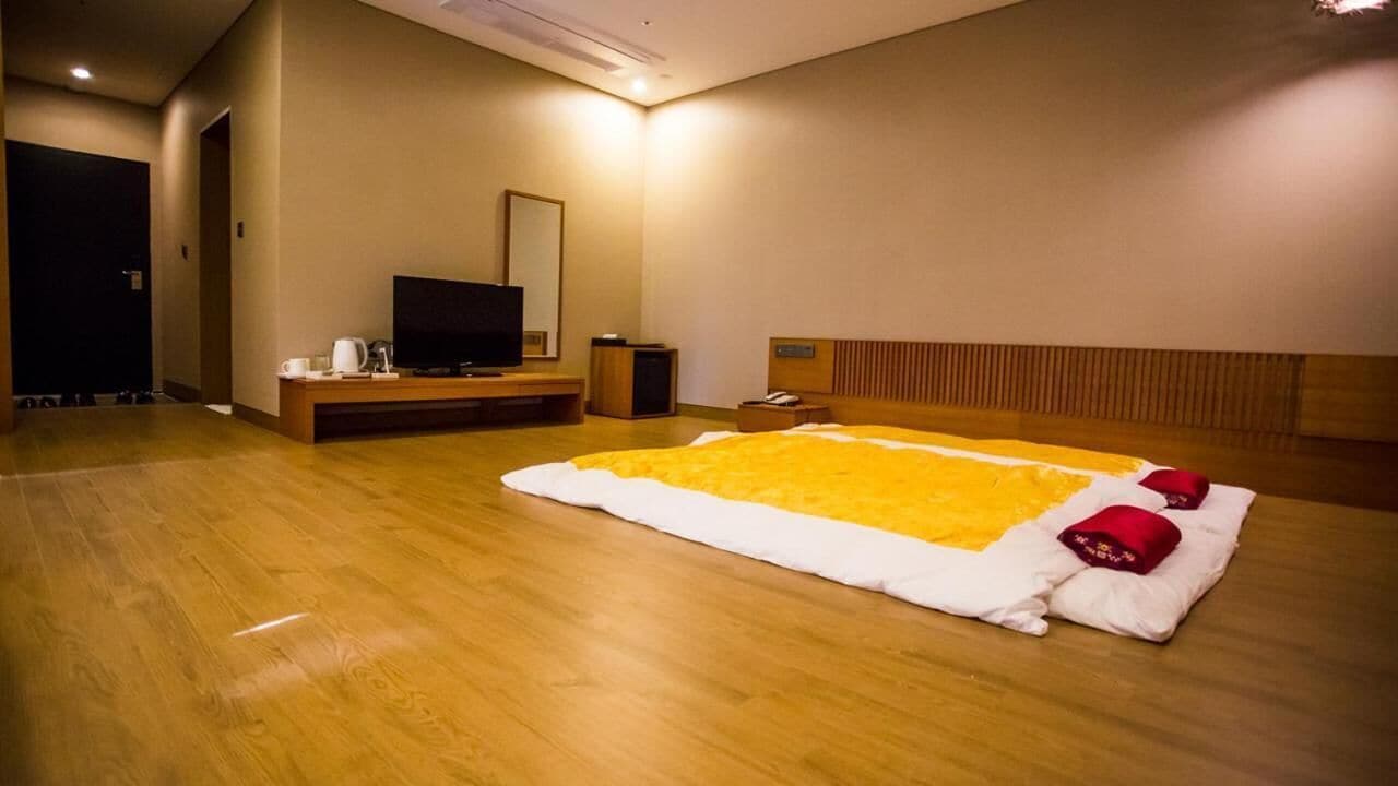 Una camera d'albergo con un letto grande, una televisione, un comodino e una testiera in legno.