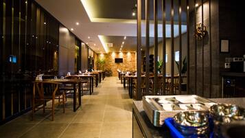 A modern restaurant with a long counter, wooden chairs, and a stone wall in the background.