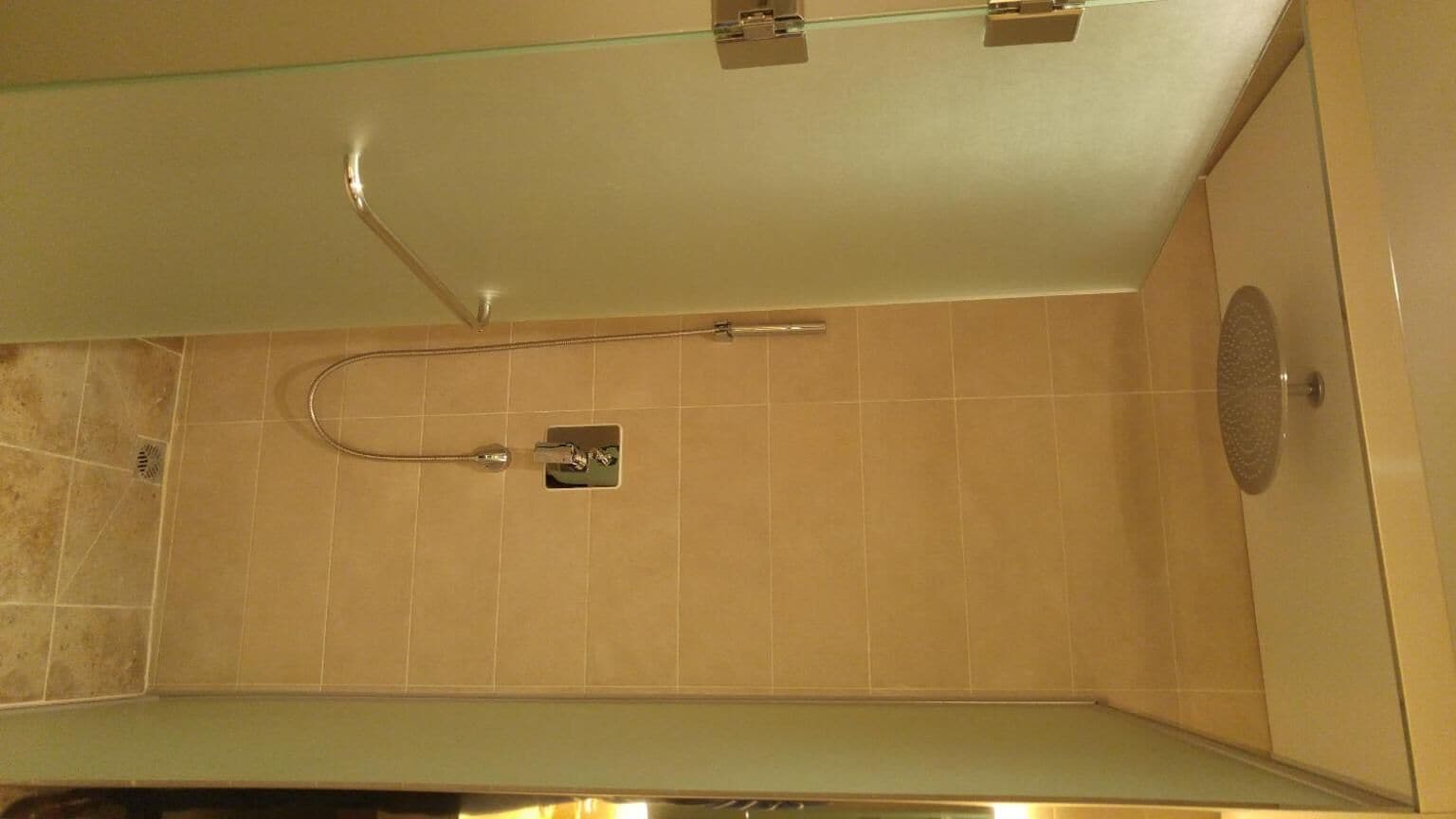 A shower with a glass door, a handheld showerhead, and a wall-mounted control panel.