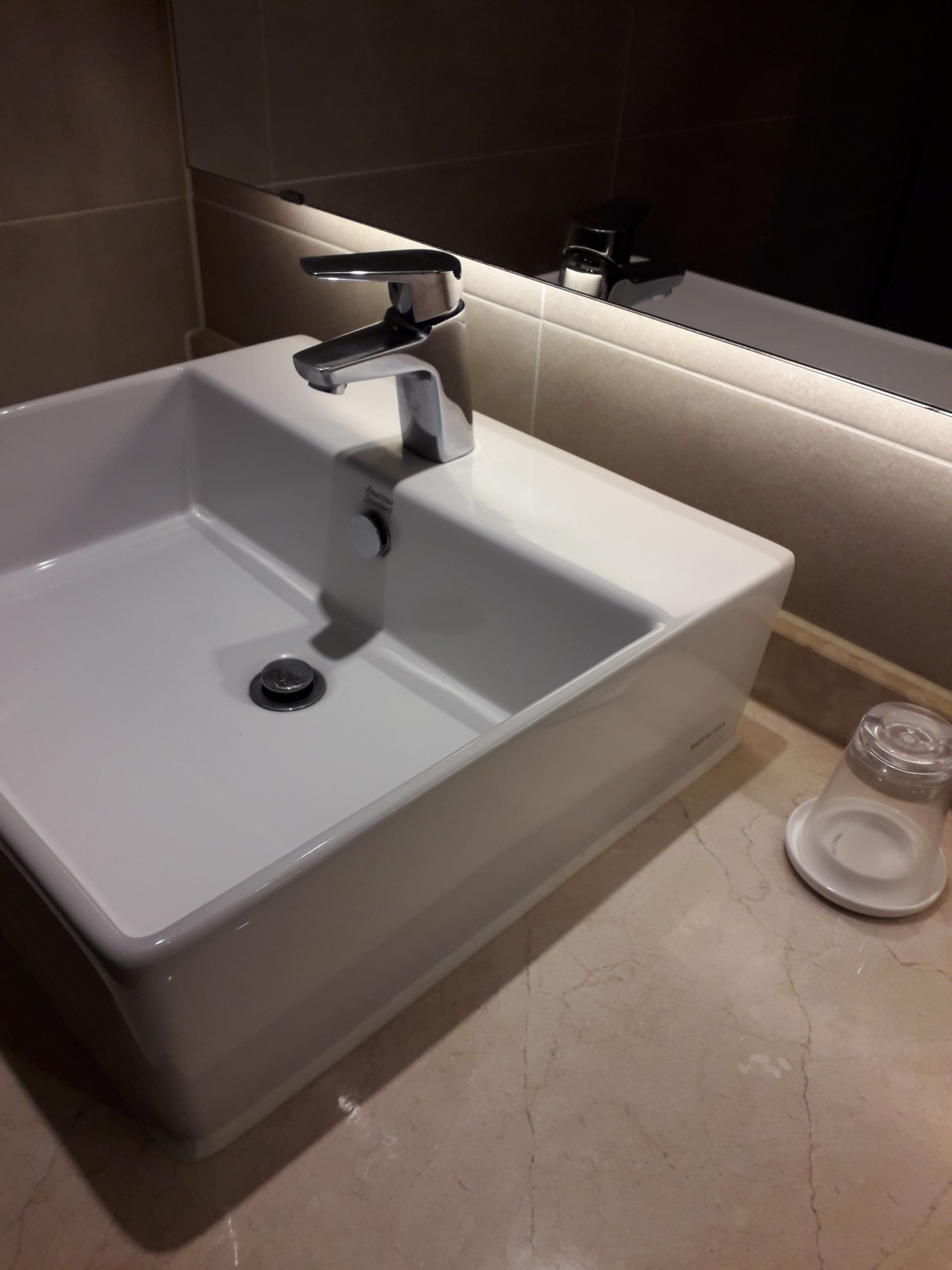 A white bathroom sink with a chrome faucet, a mirror above it, and a glass container on the countertop.