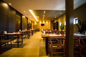 Un restaurante con varias mesas y sillas, una pared de piedra al fondo y una pantalla de televisión montada en la pared.