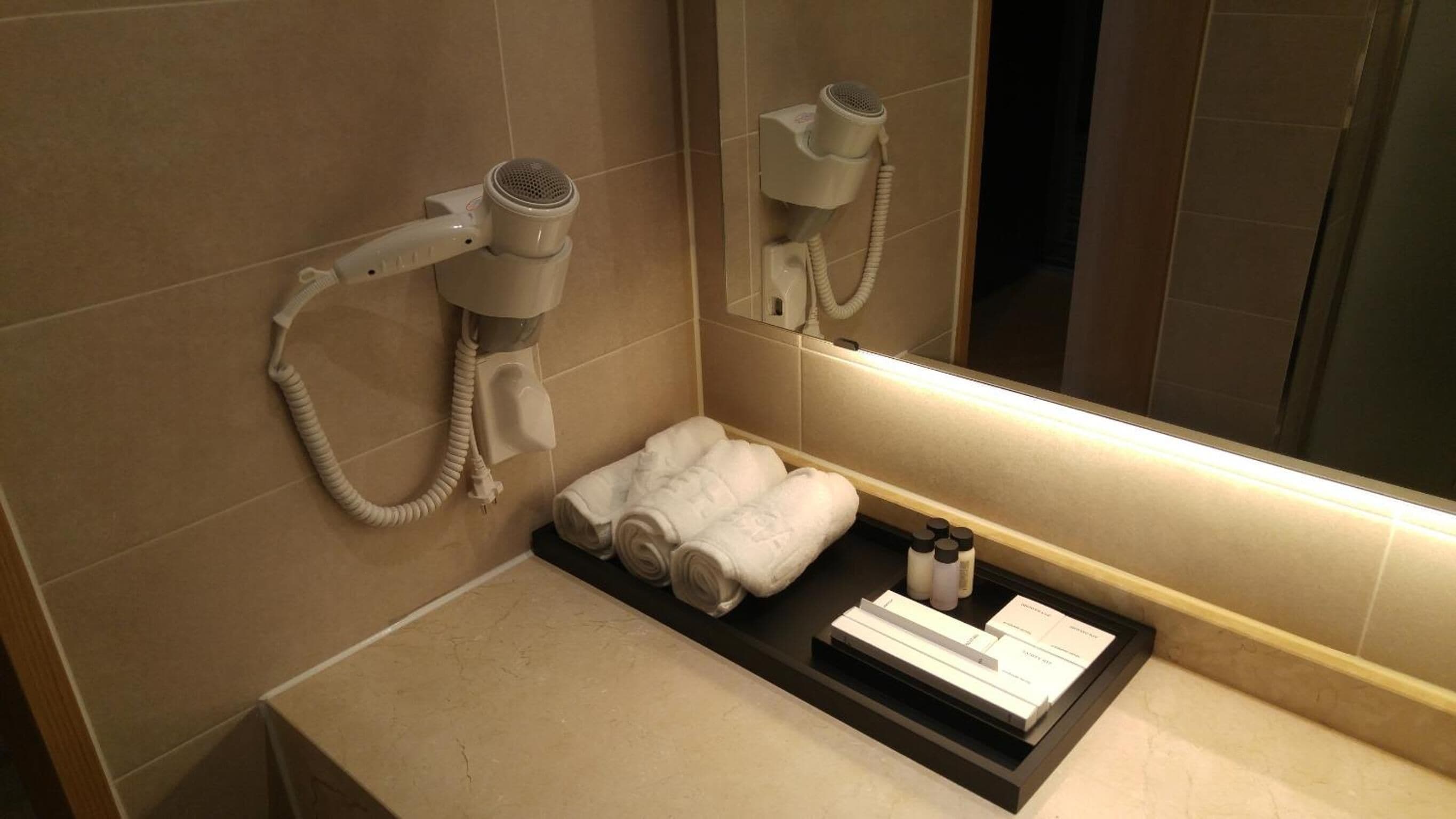 A bathroom with a hairdryer mounted on the wall, a towel rack with towels, and a shelf with toiletries.
