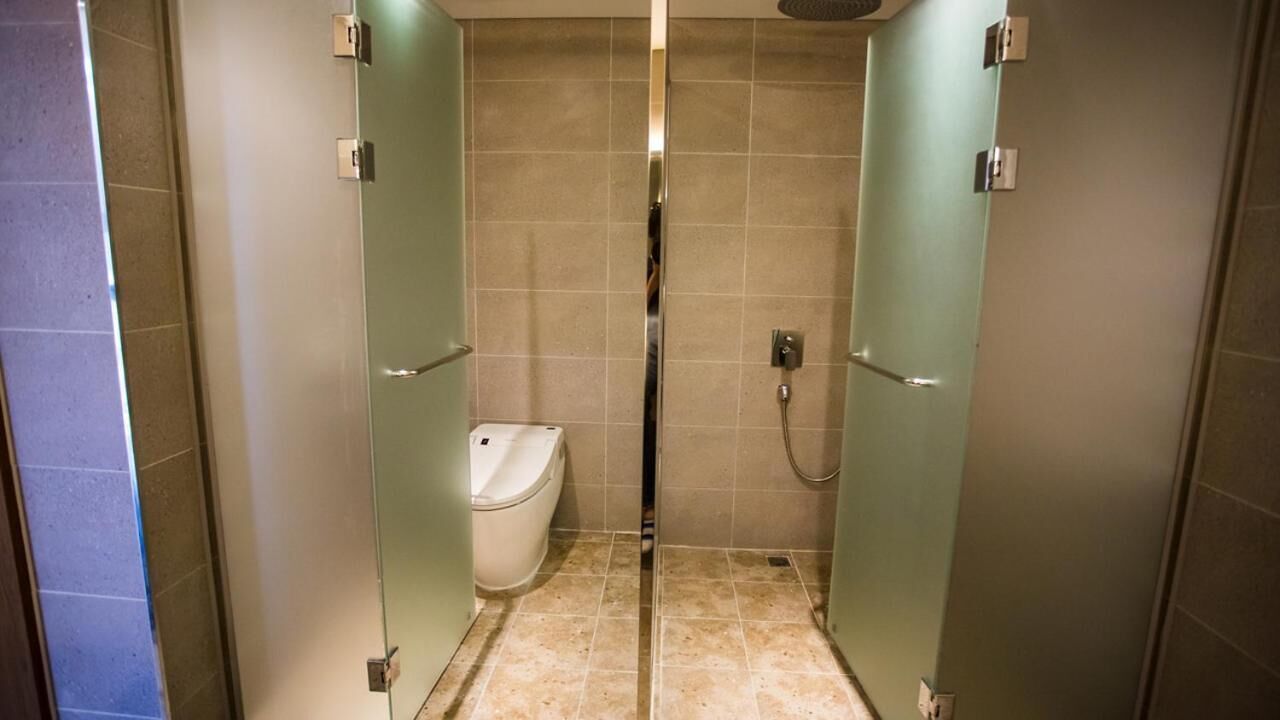 A small, enclosed shower stall with a toilet, glass doors, and a showerhead.