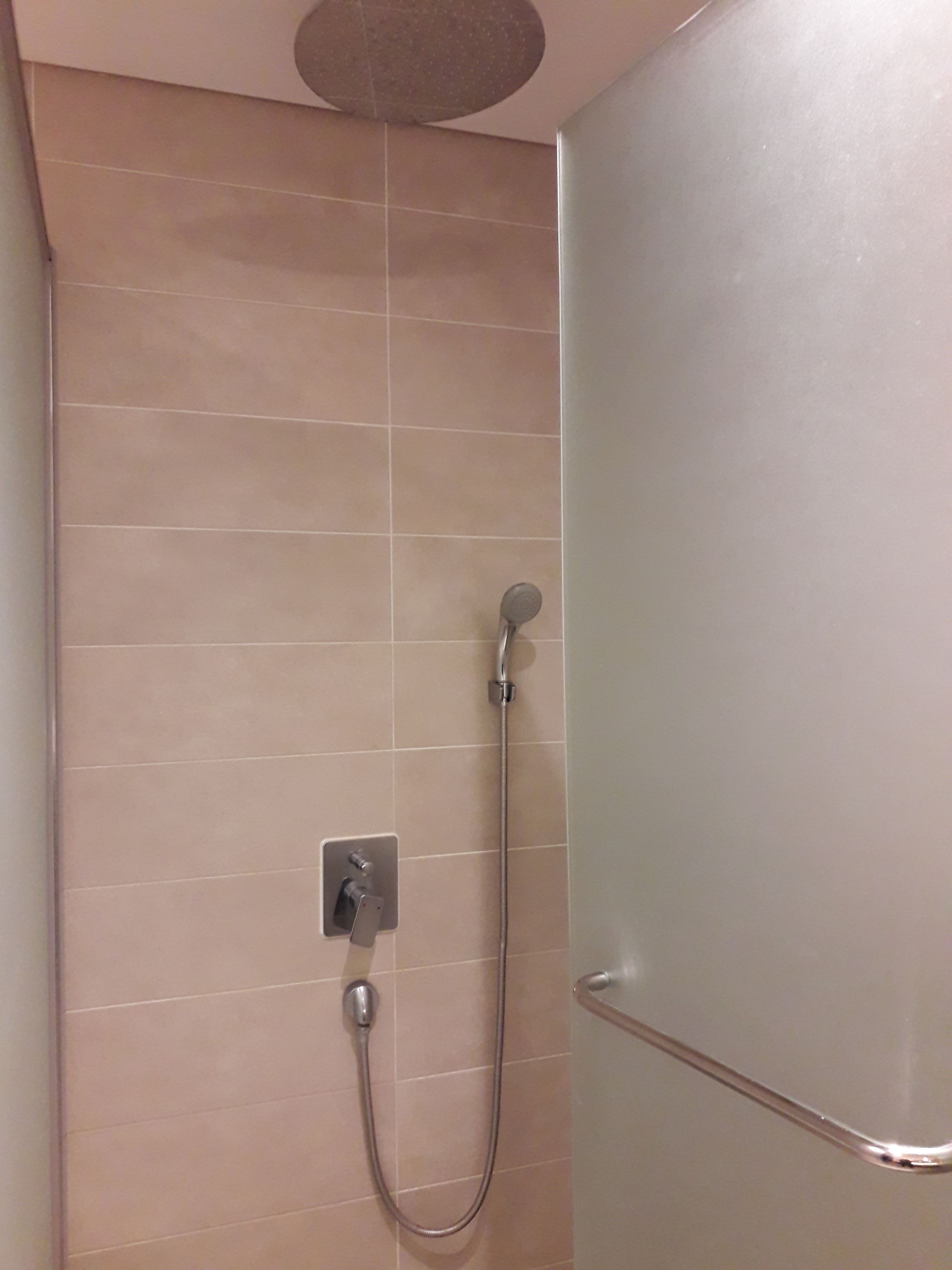 A shower with a handheld showerhead and a wall-mounted control panel.