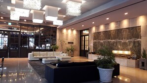 A modern lobby with a sectional sofa, a reception desk, and a large stone wall. - J Square Hotel (Jinju)