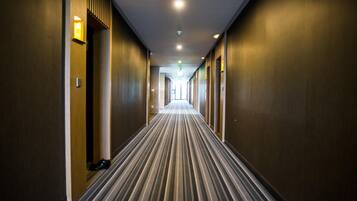 A hotel hallway with a striped carpet, wooden walls, and recessed lighting.