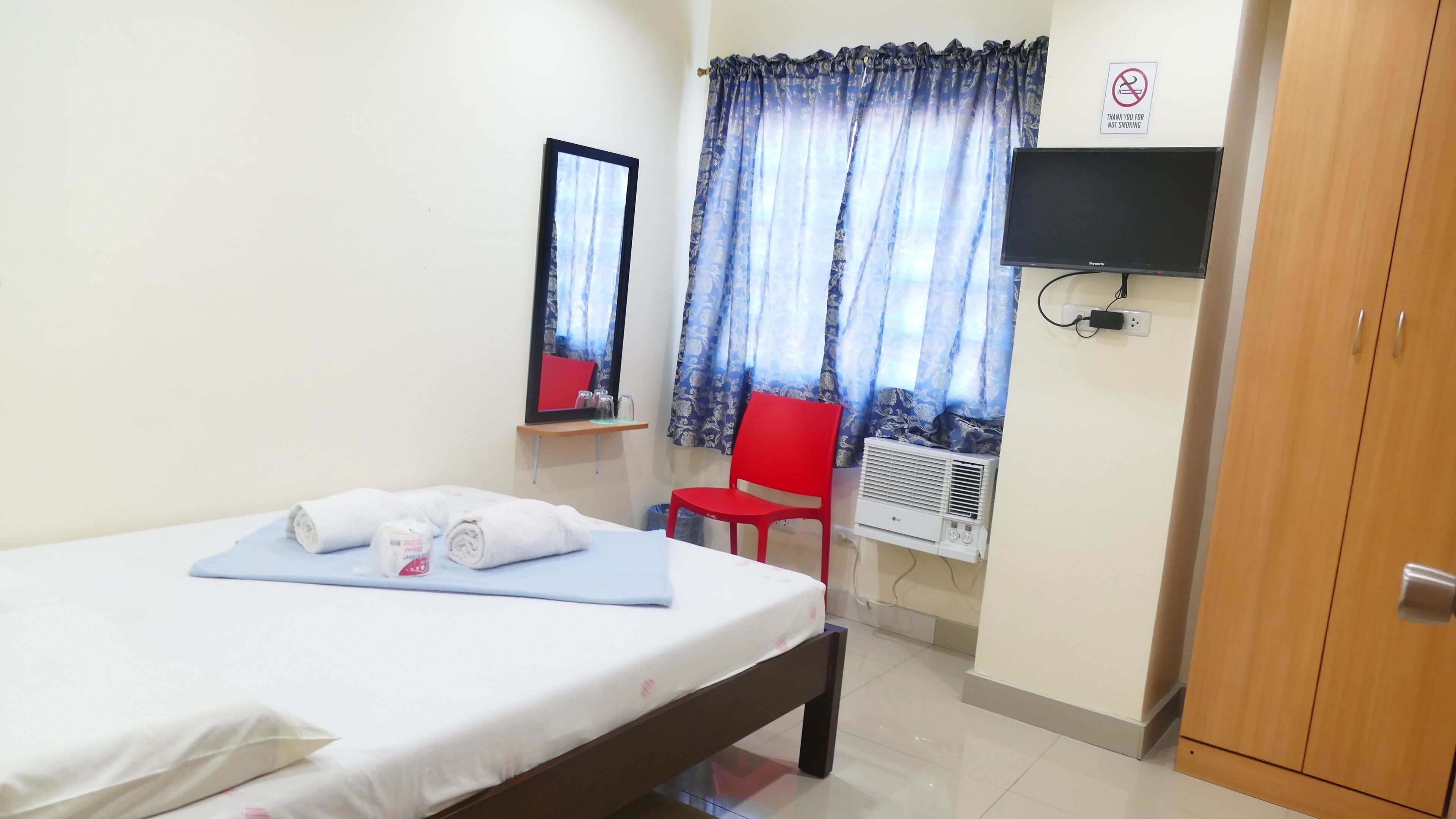 Habitación de hotel con una cama, una silla roja, un televisor y un cartel de no fumar.