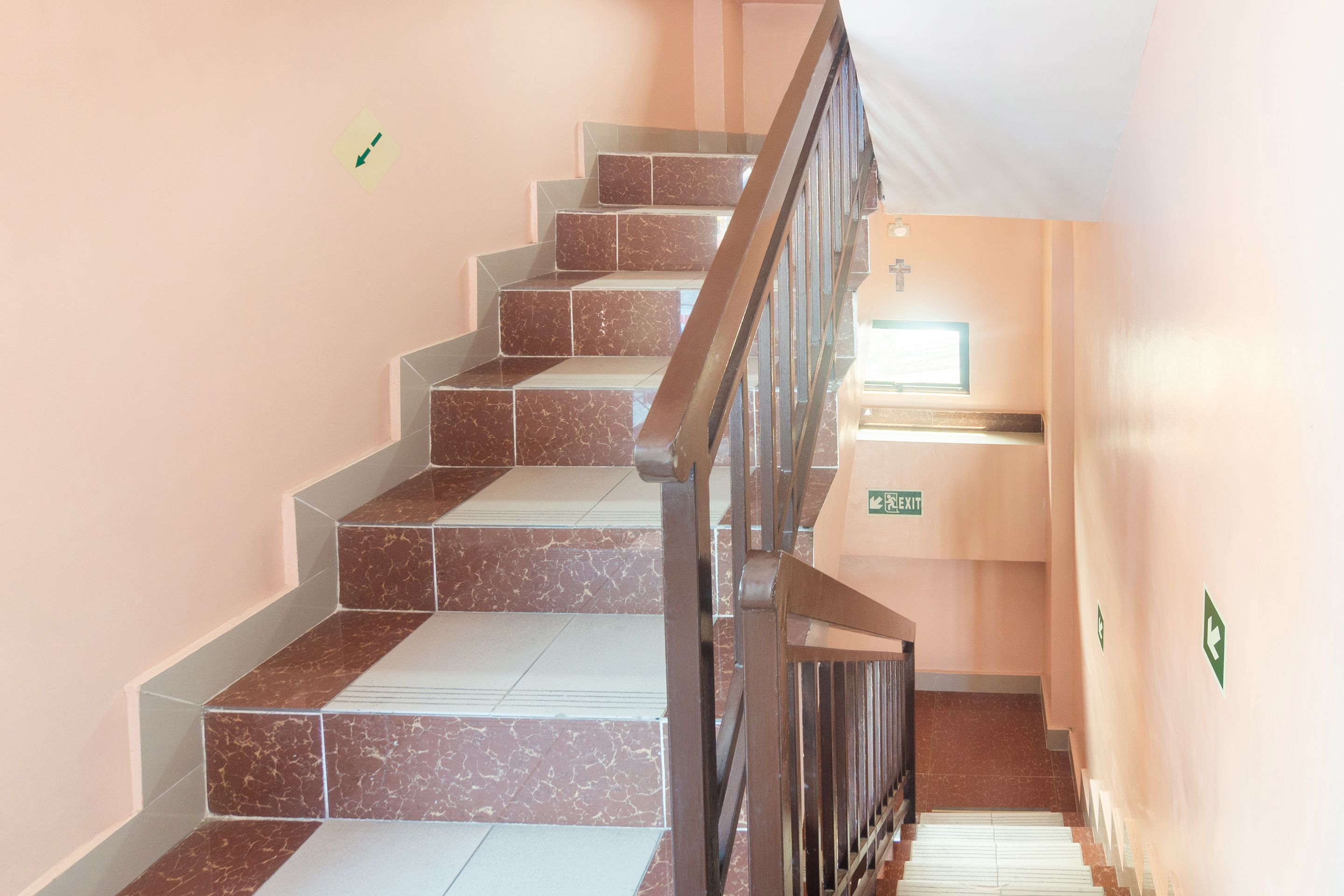 A staircase with alternating dark and light tiles, a metal railing, and green directional signs on the walls.